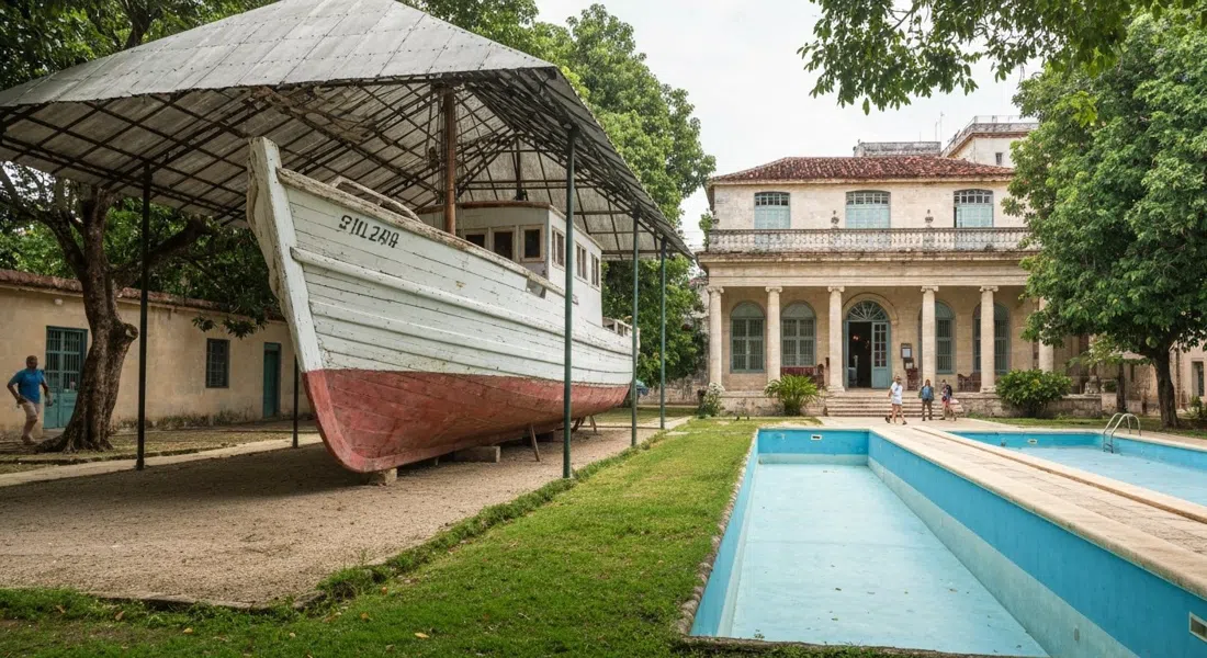 la Pilar restaurata al coperto nel giardino del Museo Hemingway Finca Vigía, con la casa di Hemingway aperta dietro e la piscina vuota vicino